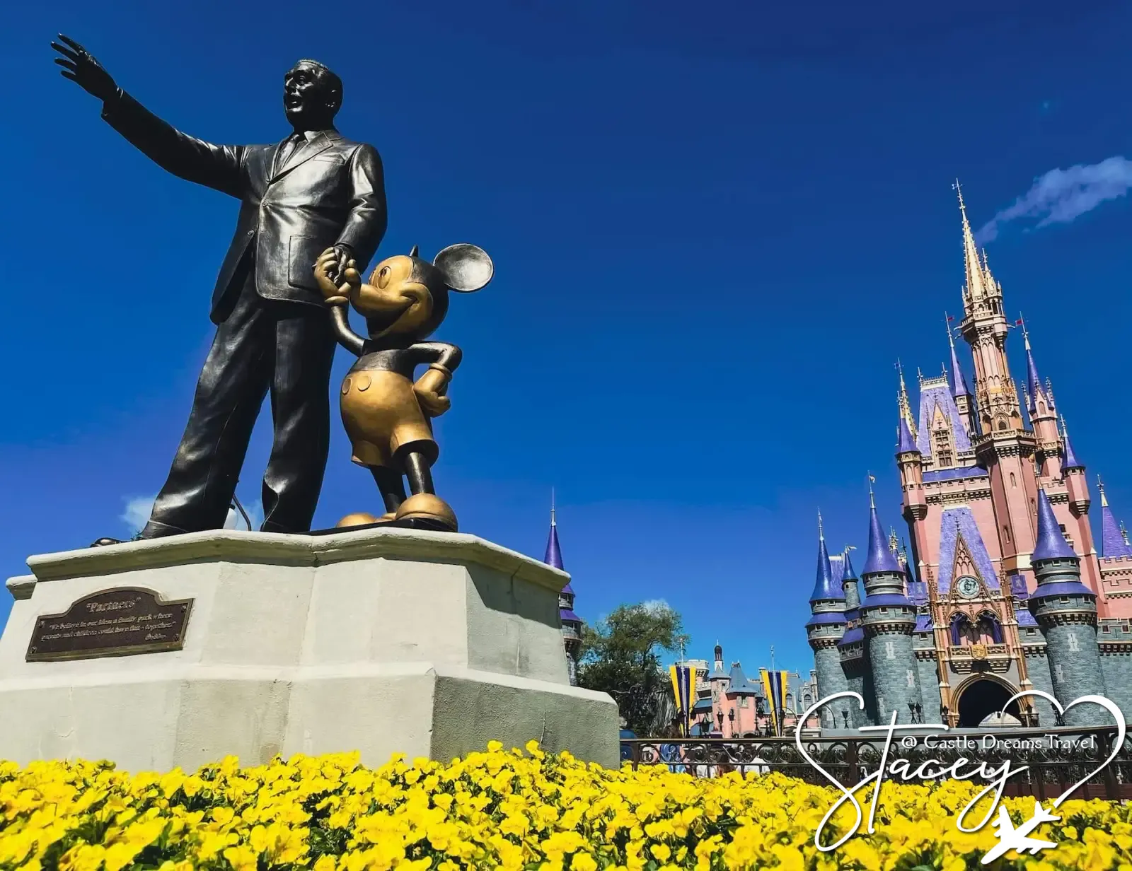 Partners statue of Walt Disney and Mickey Mouse in front of Cinderella Castle at Magic Kingdom, with yellow flowers in bloom