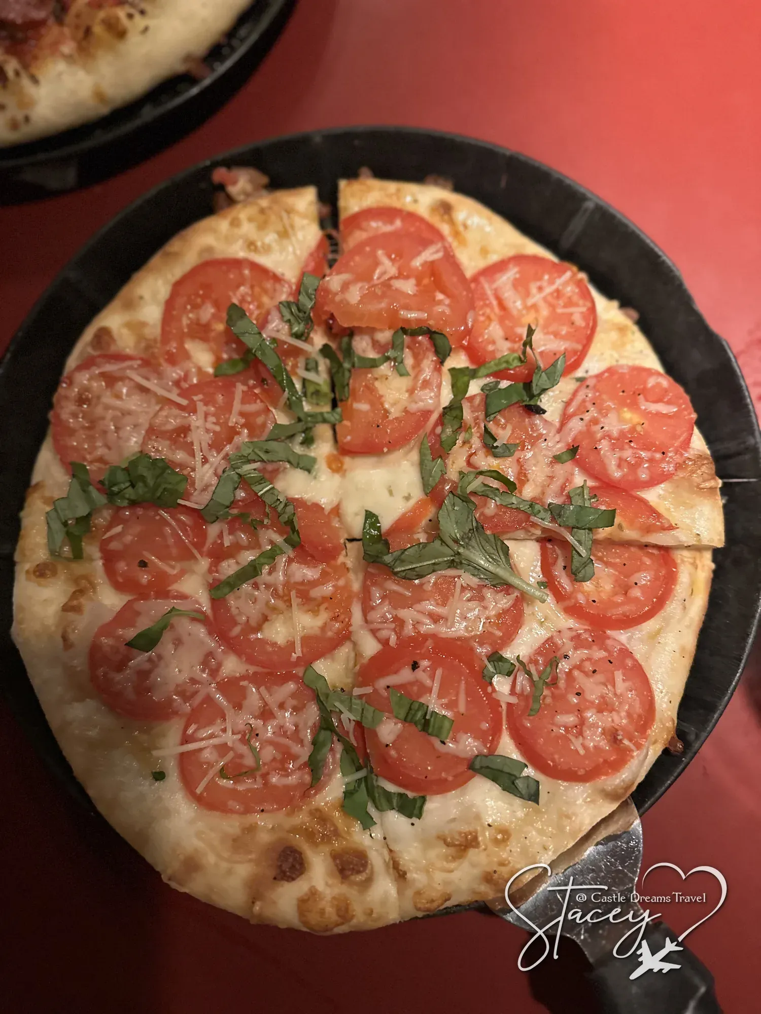 A fresh margherita pizza with sliced tomatoes and basil in a black pan