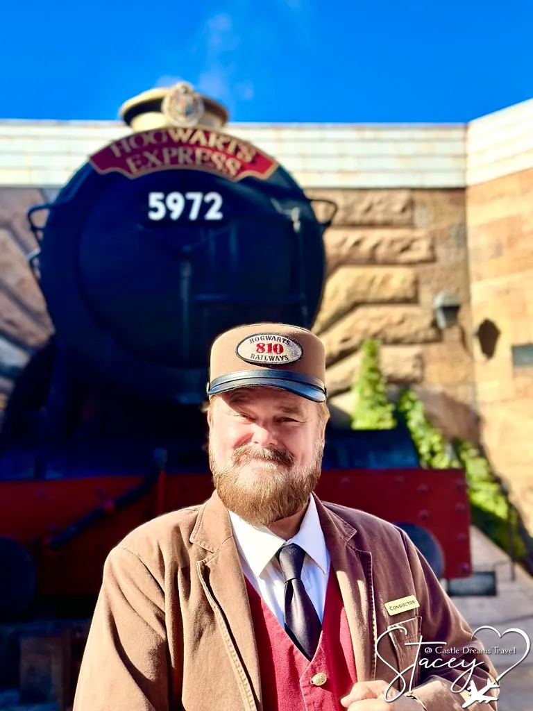 The Hogwarts Express conductor in uniform standing in front of the red and black engine