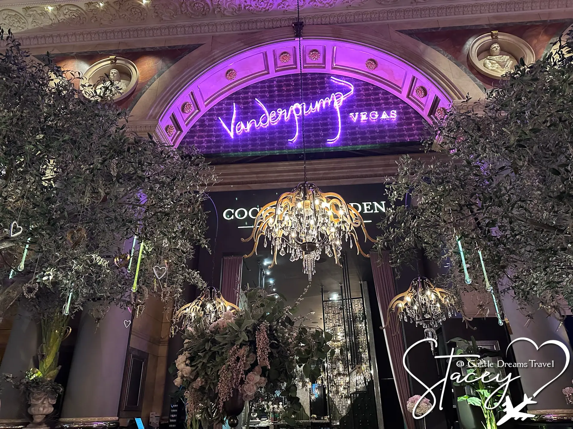 The neon Vanderpump Cocktail Garden sign glowing above the tree-filled entrance to the Cocktail Garden in Las Vegas