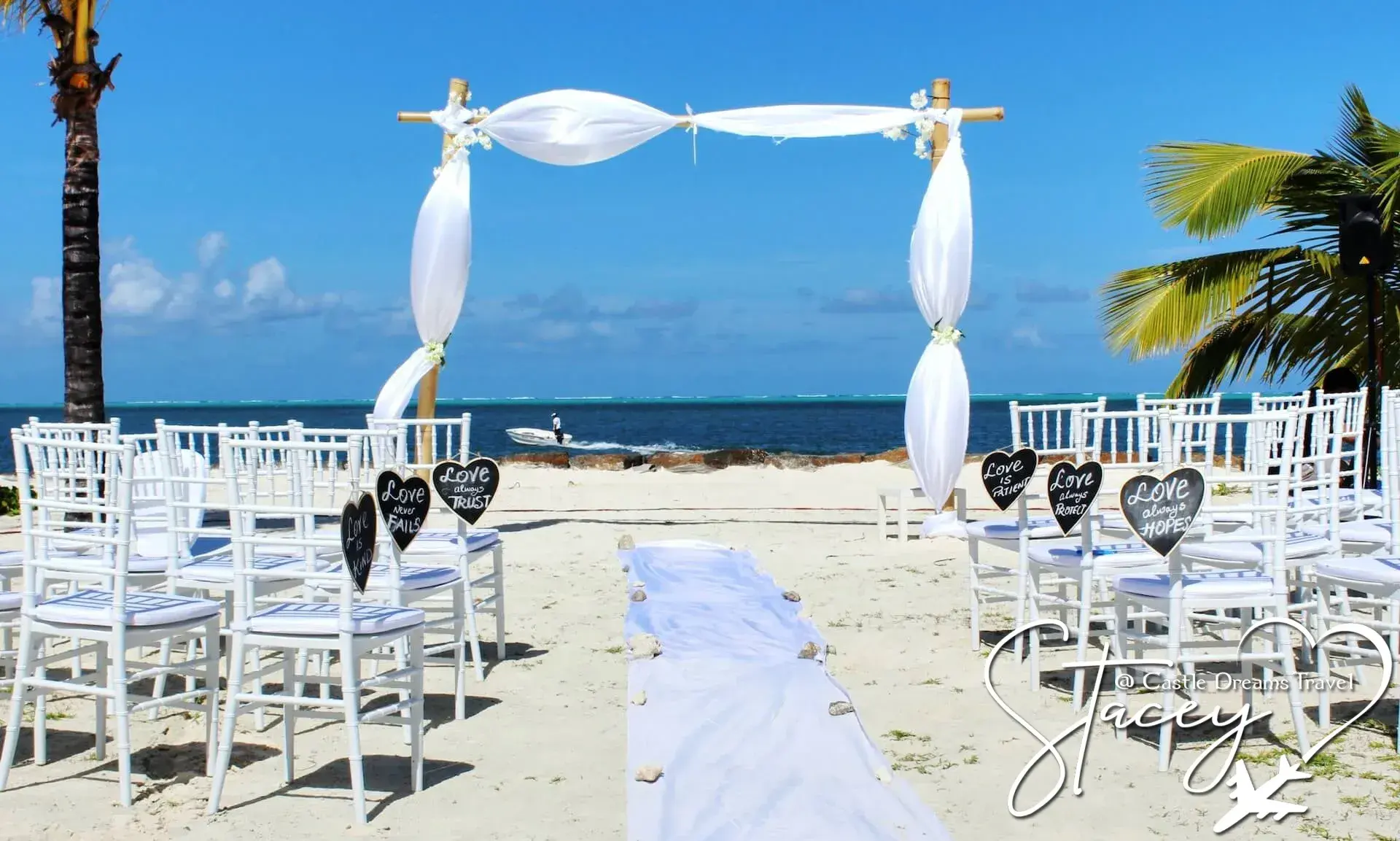 Rows of white chairs and a draped wedding arch set up for a beach ceremony