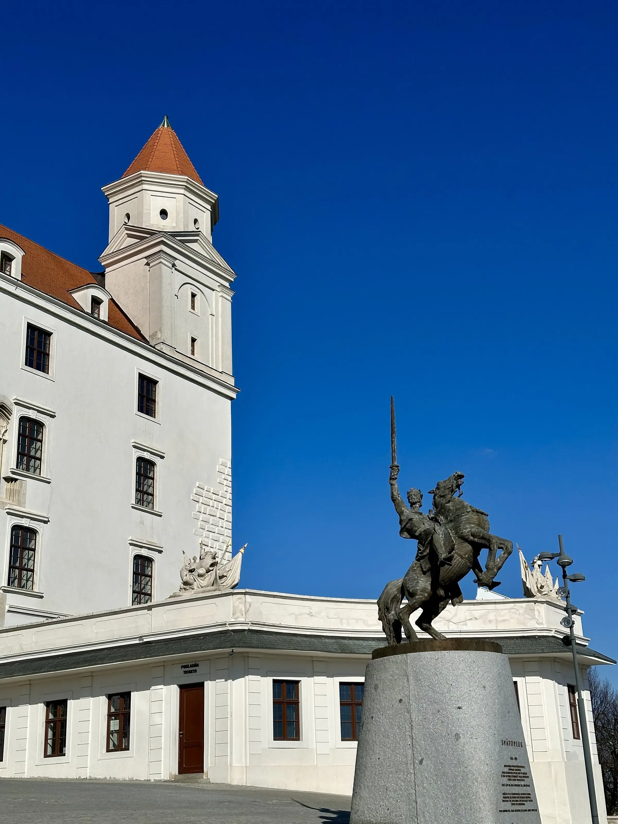 Bratislava Castle's white walls and red roof beside the bronze equestrian statue of Svätopluk