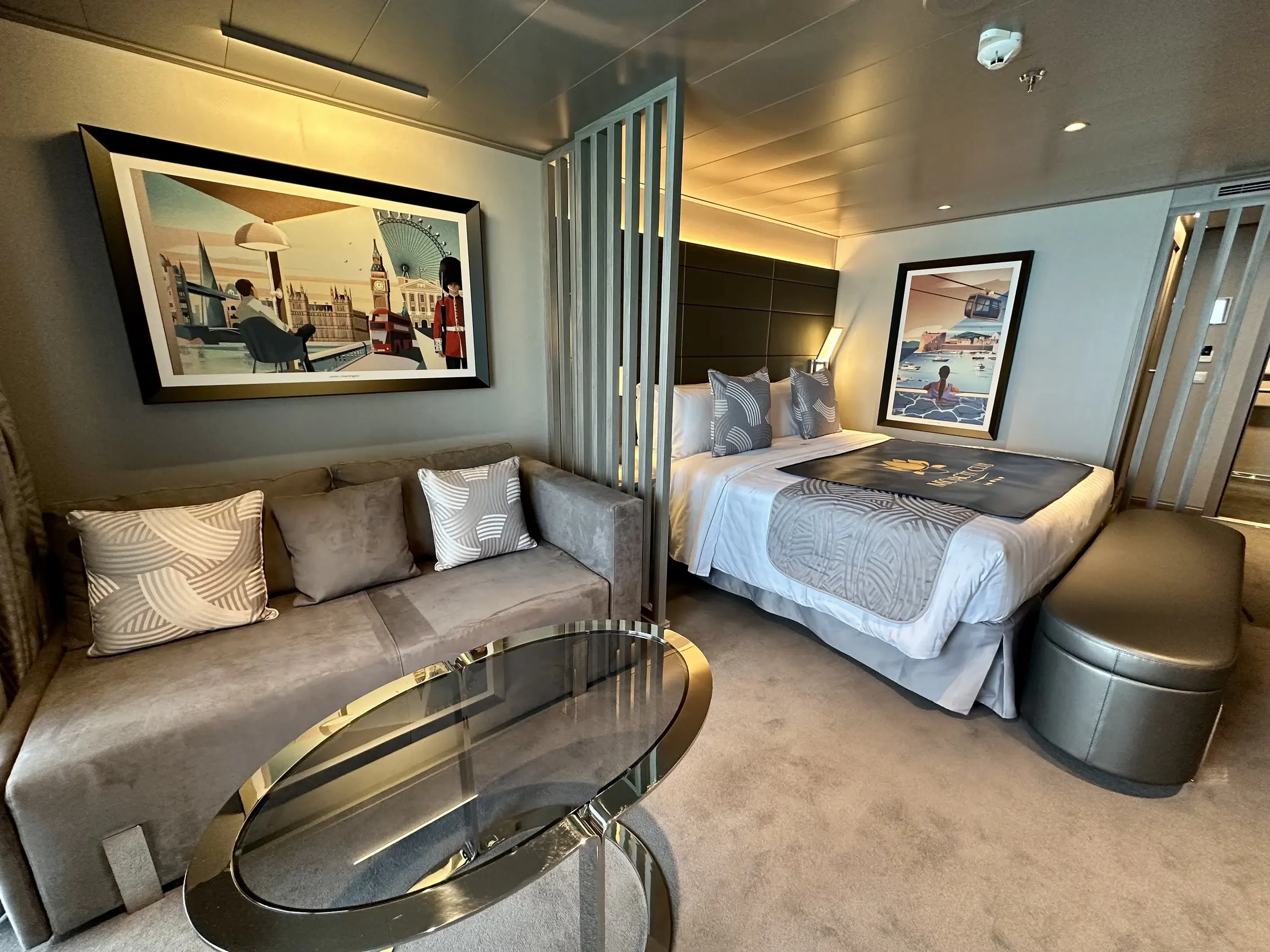 An MSC Yacht Club suite with a sofa, artwork and the bed beyond