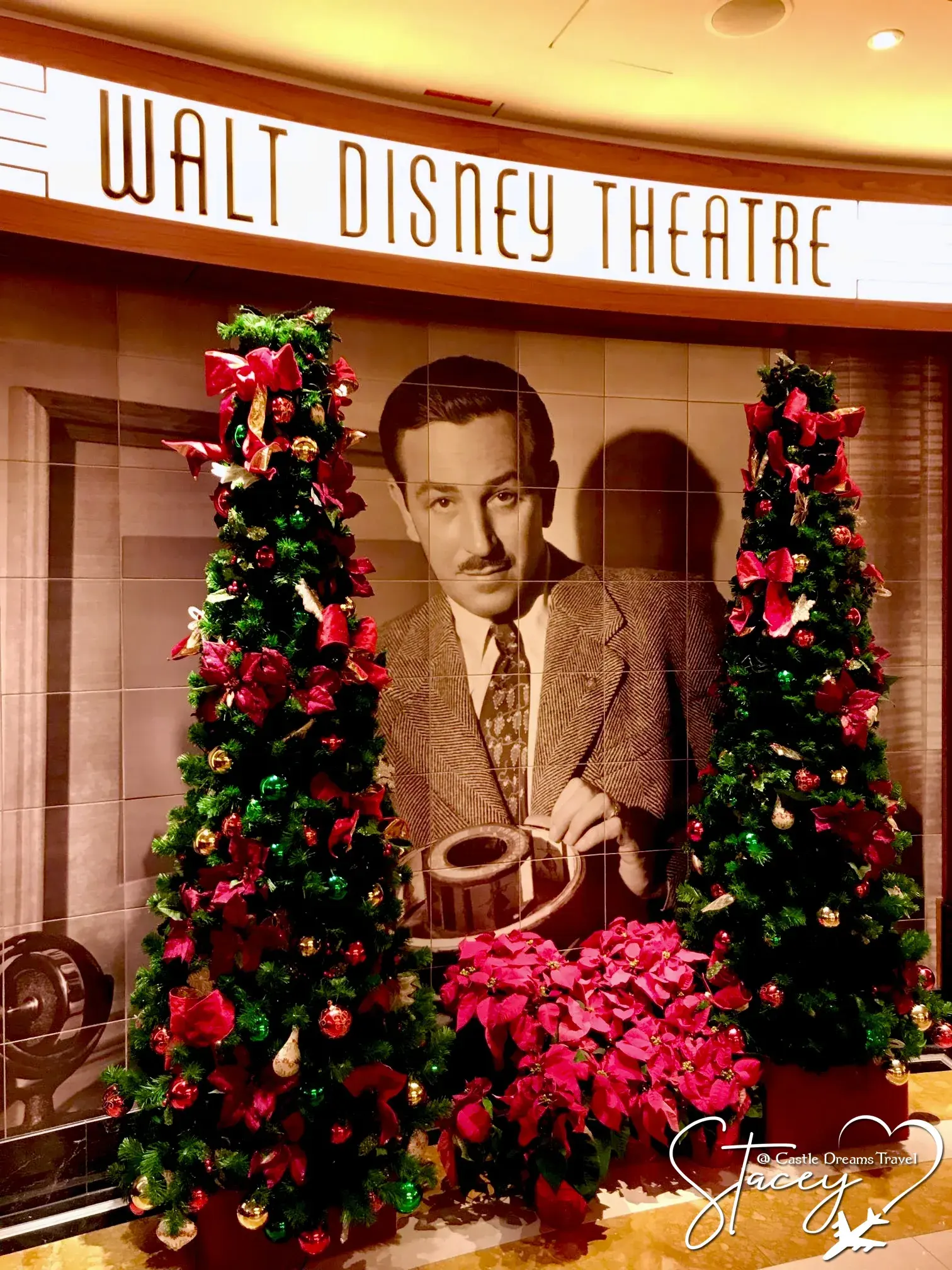 Christmas trees and poinsettias framing the Walt Disney portrait outside the Walt Disney Theatre on a Disney cruise ship