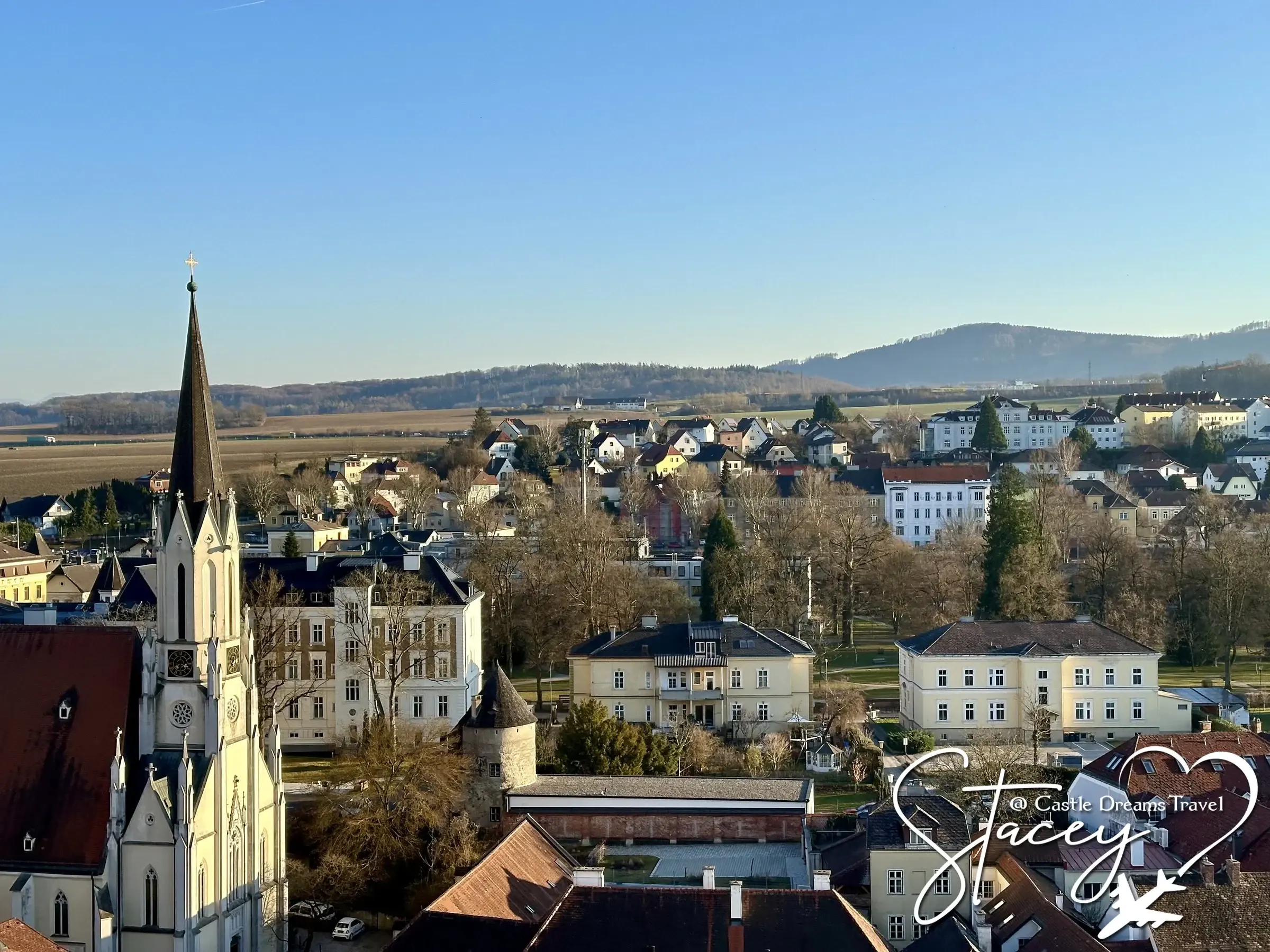 The rooftops and church spire of Melk town below the abbey, with hills beyond