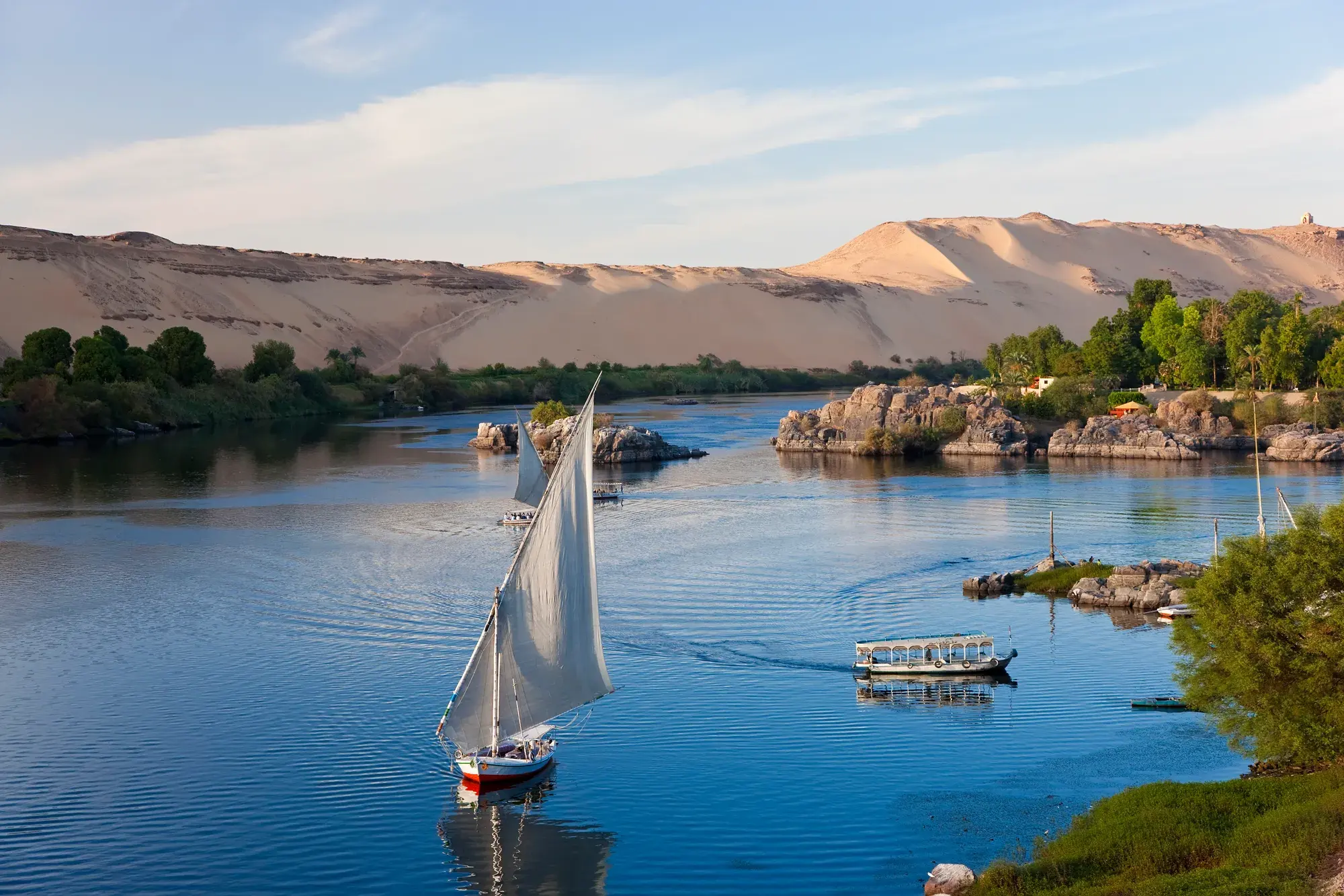 A felucca sailboat and tour boat on the Nile River through the Egyptian desert near Aswan